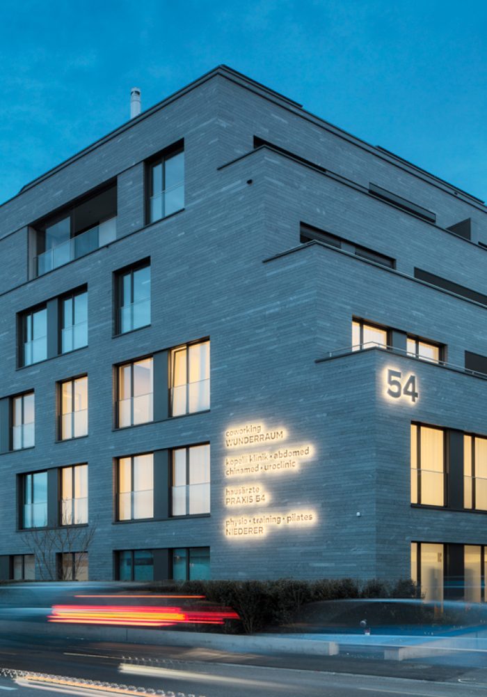Wohn- und Geschäftshaus mit Steinfassade und leuchtender Hausnummer 54 in der Dämmerung